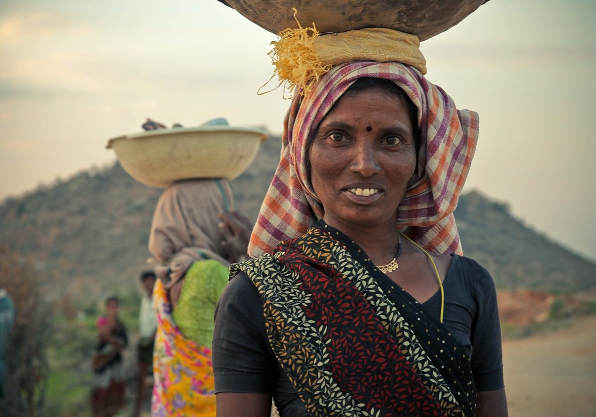 Mit offenem Blick schaut die indische Frau, die ihre Lasten auf dem Kopf transportiert, in die Kamera